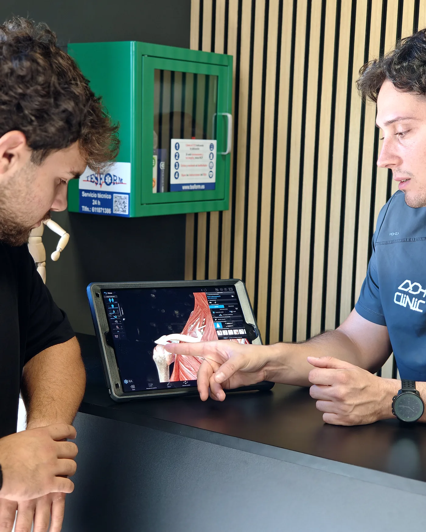Fisioterapeuta de ADH Clinic explicando el diagnóstico sobre un atlas de anatomía